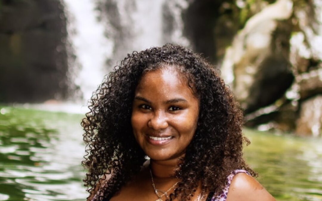 A picture of a woman with curly hair in front of a waterfall