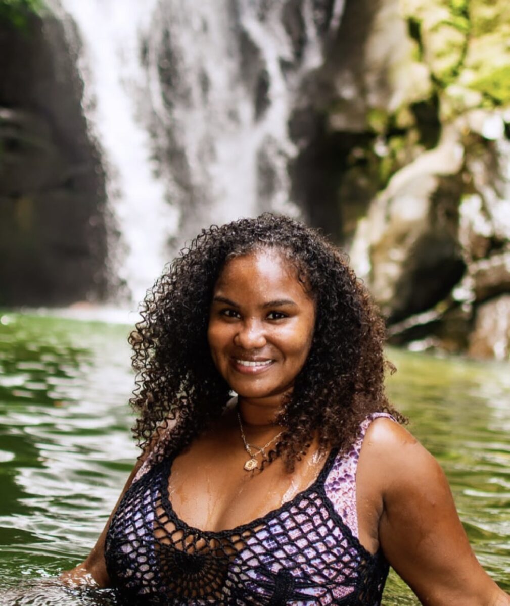 A picture of a woman with curly hair in front of a waterfall